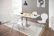 Moderner Esstisch mit weißer Tischplatte und Metallgestell, umgeben von vier weißen Stühlen in einem hellen Esszimmer mit Holzfußboden, aus seitlicher Perspektive fotografiert.