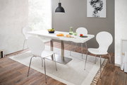 Moderner Esstisch mit weißer Tischplatte und Metallgestell, umgeben von vier weißen Stühlen in einem hellen Esszimmer mit Holzfußboden, aus seitlicher Perspektive fotografiert.