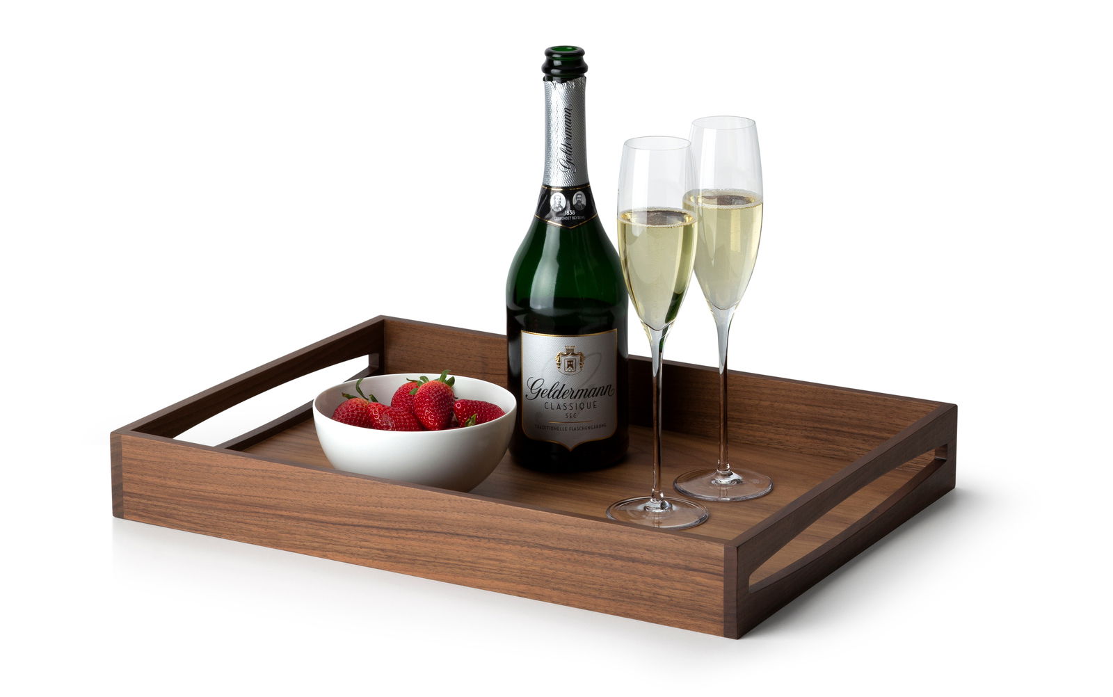 Tablett aus Walnussholz mit einer Flasche Sekt, zwei gefüllten Sektgläsern und einer Schale Erdbeeren, seitliche Perspektive.
