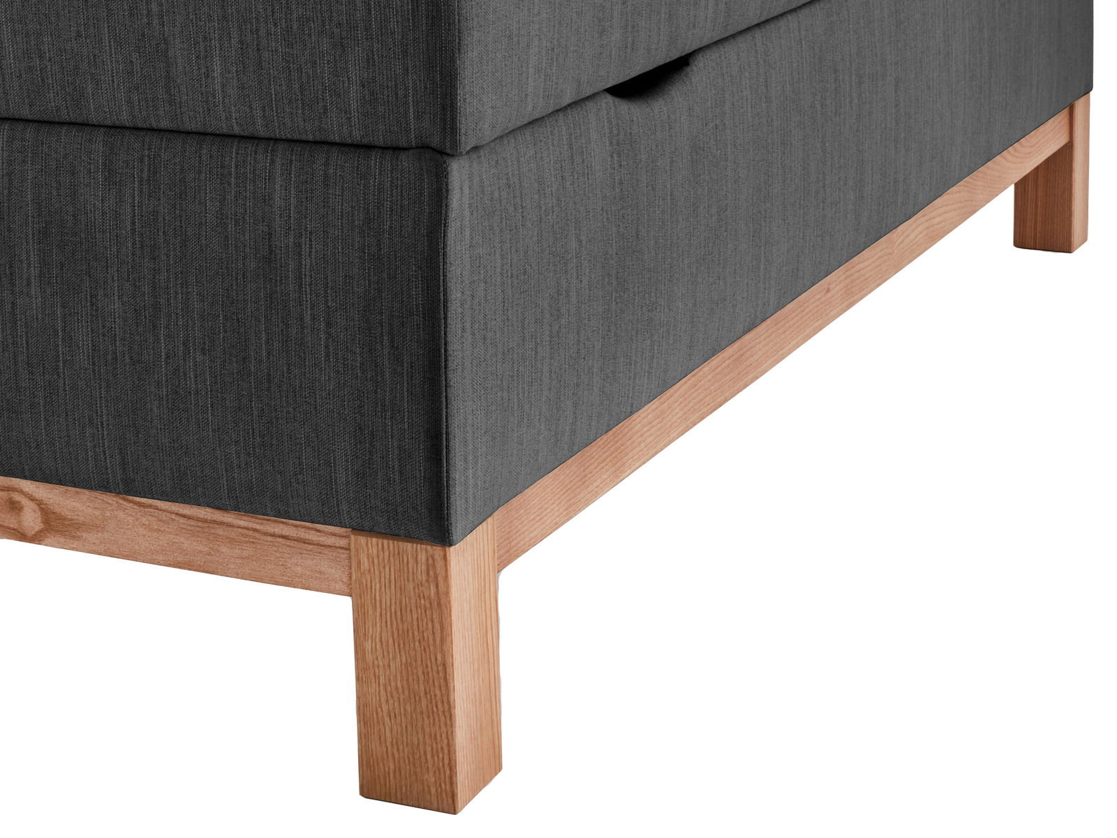 Nahaufnahme eines Boxspringbetts mit grauem Stoffbezug und Holzfüßen, seitliche Perspektive.