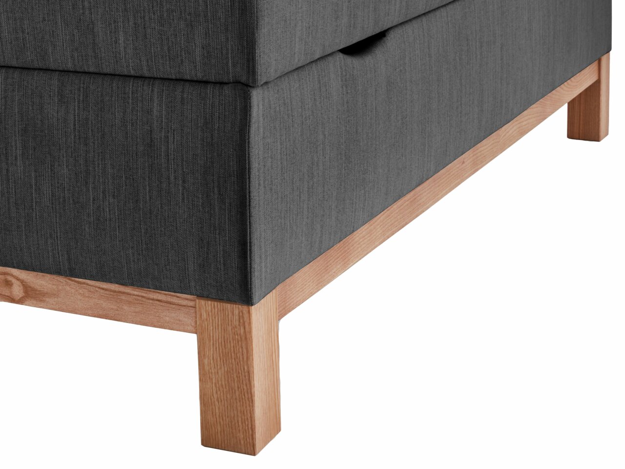 Nahaufnahme eines Boxspringbetts mit grauem Stoffbezug und Holzfüßen, seitliche Perspektive.
