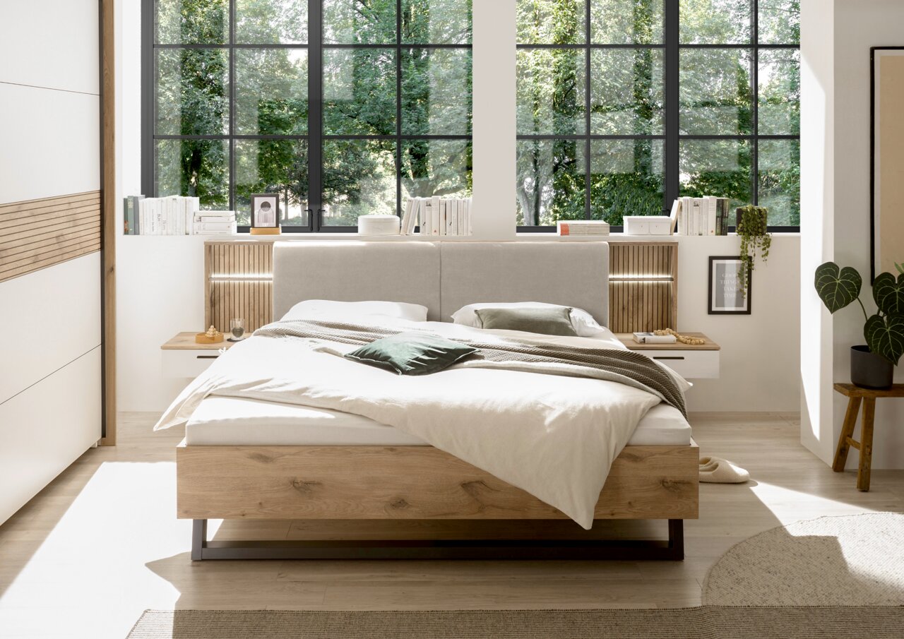 Modernes Schlafzimmer mit einem stilvollen Bett in Holzoptik, umgeben von großen Fenstern mit Blick ins Grüne. Frontalansicht.