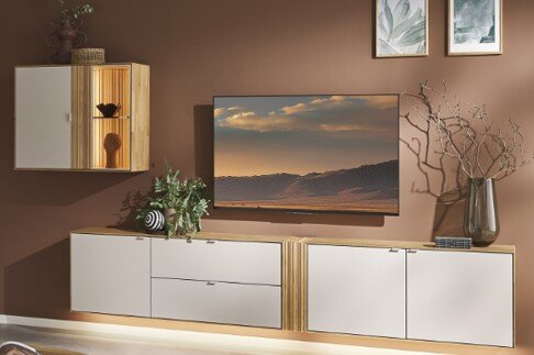 Modernes Wohnzimmer-Set mit niedrigem TV-Board in Weiß und Holzoptik, mittig platzierter Flachbild-TV und passendem Hängeschrank links; Frontansicht leicht schräg von vorne.