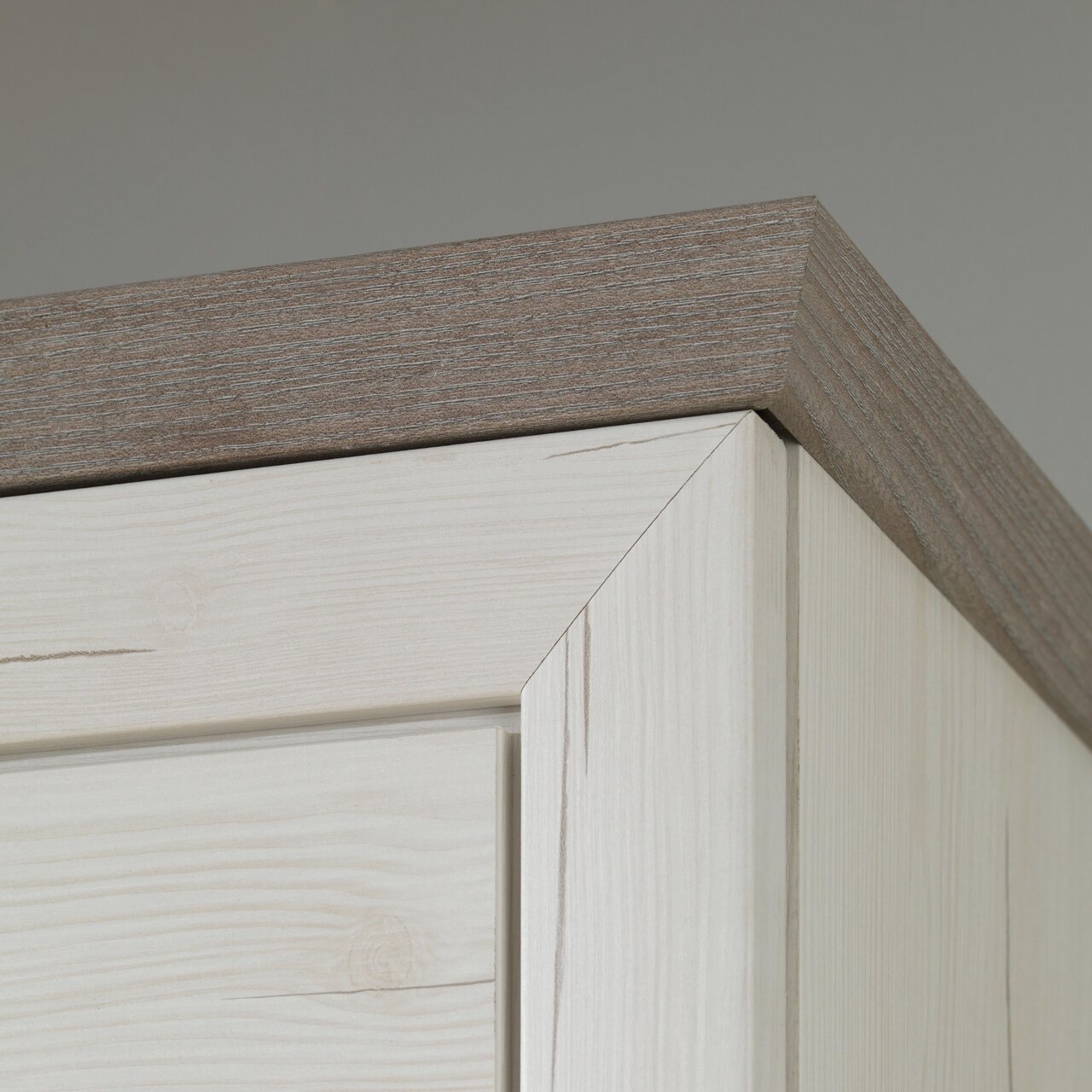 Close-up van de bovenhoek van een schoenenkast van licht hout met een donkerdere houten rand, gezien van onderaf.