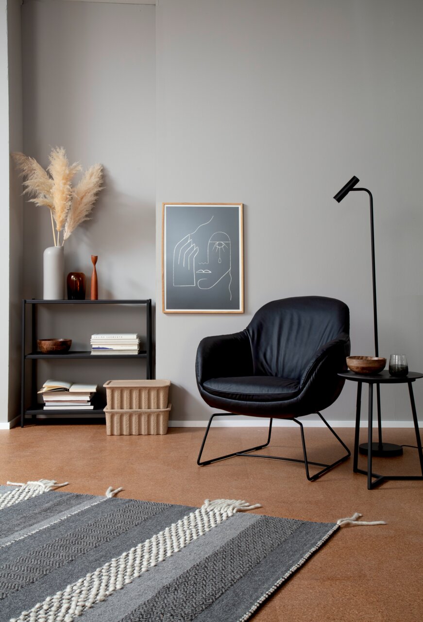 Moderne bijzettafel van zwart metaal, naast een zwarte fauteuil, versierd met een houten schaal en glas.