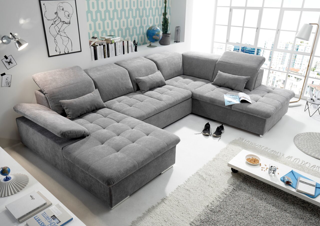 Graue Wohnlandschaft in U-Form mit verstellbaren Kopfstützen und Kissen, in einem modernen Wohnzimmer mit großen Fenstern und stilvoller Dekoration. Perspektive von oben links.