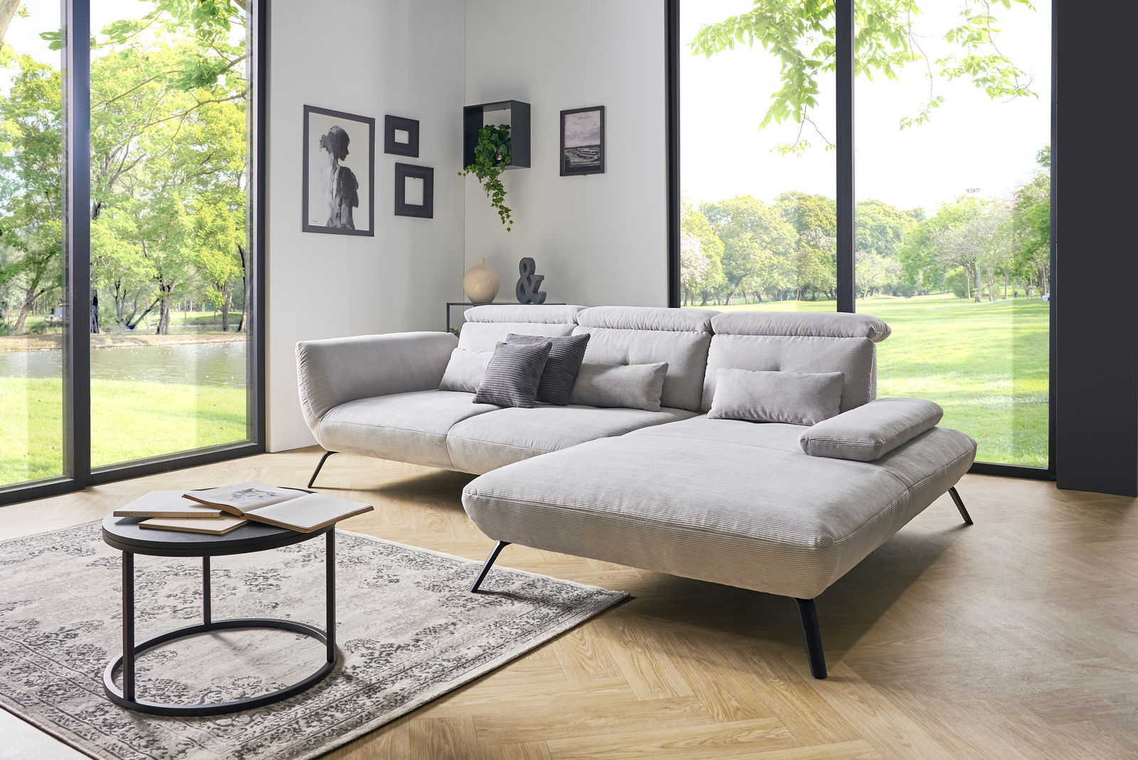 Moderne Rundecke in einem hellen Wohnzimmer mit großen Fenstern, die einen Blick ins Grüne bieten. Perspektive von vorne links.