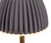 Nahaufnahme eines schwarzen, plissierten Lampenschirms mit warm leuchtender Kante und sichtbarem Lampenfuß, fotografiert aus leicht seitlicher Frontperspektive.