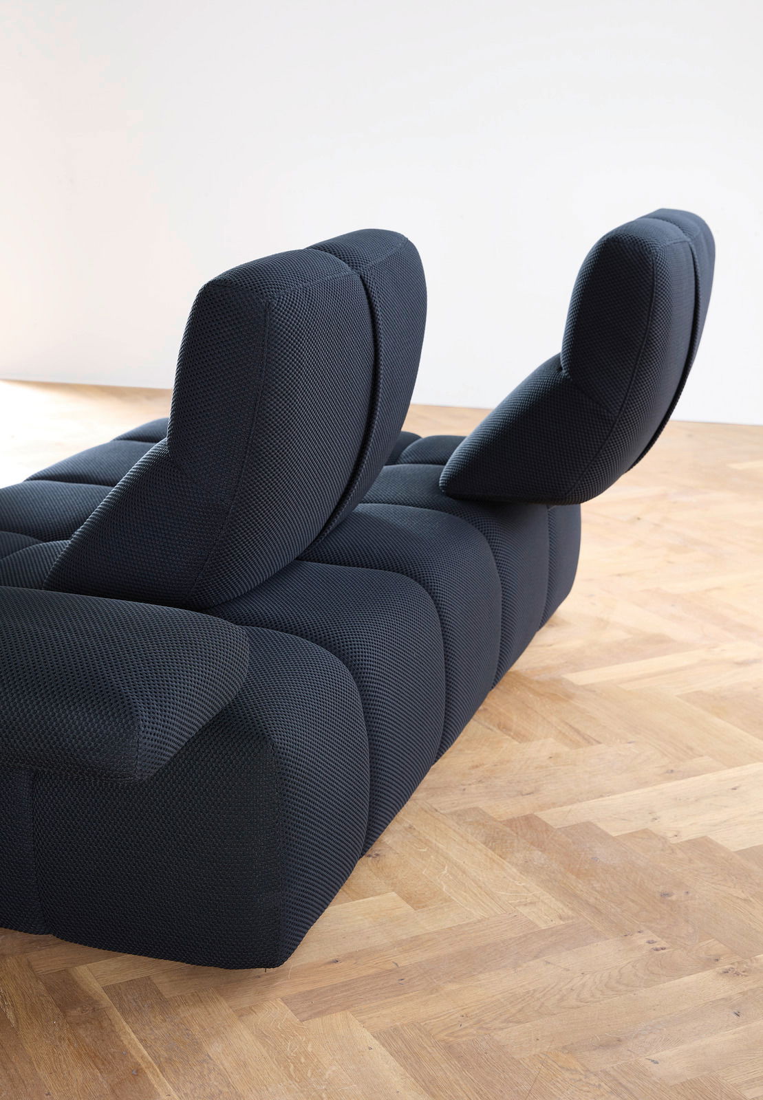 Rückansicht einer modernen, dunkelblauen Eckgarnitur mit verstellbaren Rückenlehnen auf einem Holzboden.