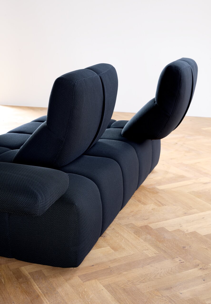 Achterkant van een moderne, donkerblauwe hoekbank met verstelbare rugleuningen op een houten vloer.