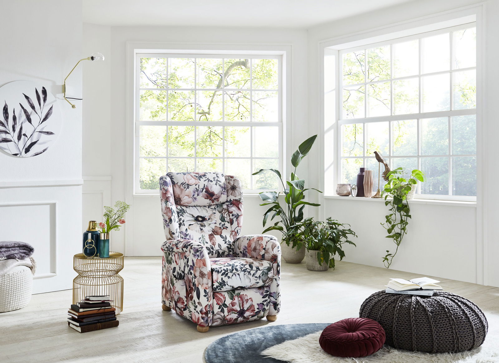 Blumiger Fernsehsessel in einem hellen Wohnzimmer mit großen Fenstern und Pflanzen, seitliche Perspektive