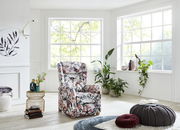 Blumiger Fernsehsessel in einem hellen Wohnzimmer mit großen Fenstern und Pflanzen, seitliche Perspektive