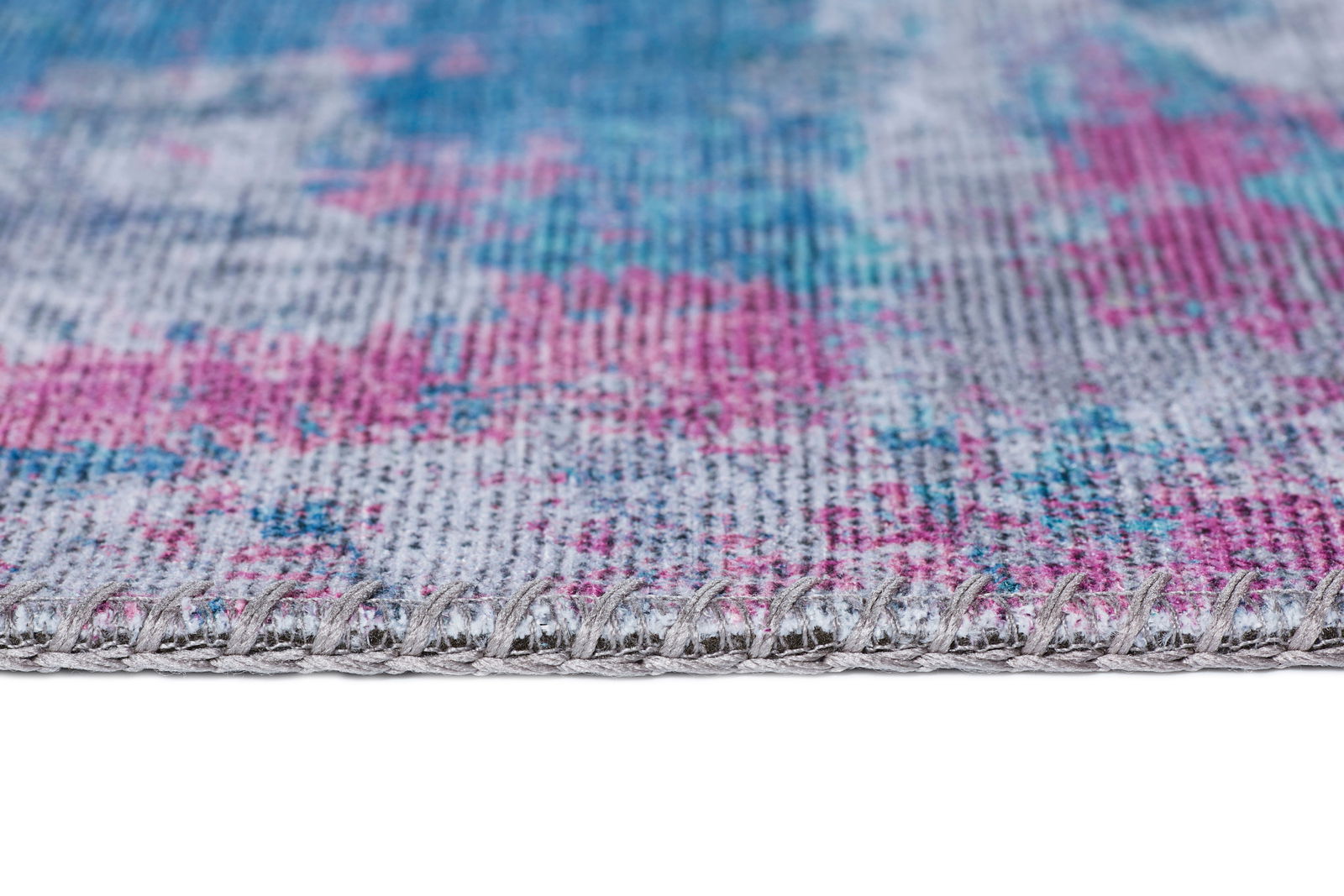 Nahaufnahme eines Teppichs mit buntem Muster in Blau- und Pinktönen, seitliche Perspektive.