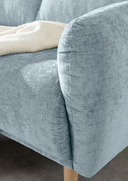 Nahaufnahme einer hellblauen Sofaecke mit abgerundeter Armlehne und Holzfuß, von der Seite betrachtet.