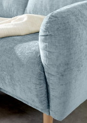 Nahaufnahme einer hellblauen Sofaecke mit abgerundeter Armlehne und Holzfuß, von der Seite betrachtet.