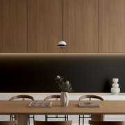 Moderne, kugelförmige Pendelleuchte in Weiß mit schwarzem Ring vor Holzpaneel-Wand über Esstisch; Frontalansicht auf Augenhöhe.