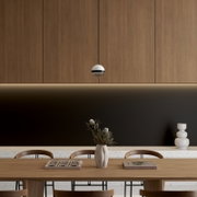 Moderne, kugelförmige Pendelleuchte in Weiß mit schwarzem Ring vor Holzpaneel-Wand über Esstisch; Frontalansicht auf Augenhöhe.