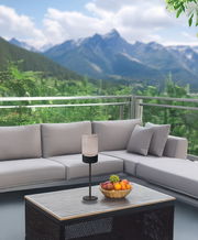 Akku-Windlicht auf einem Tisch in einem modernen Außenbereich mit Bergblick, seitliche Perspektive.