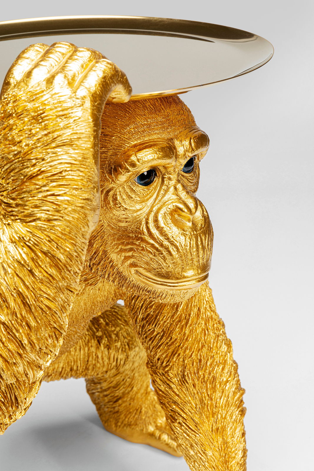 Goldene Deko-Figur eines Schimpansen in Butler-Pose, der ein Tablett auf dem Kopf balanciert. Perspektive von schräg vorne.