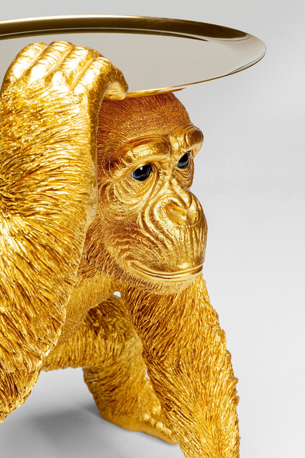 Goldene Deko-Figur eines Schimpansen in Butler-Pose, der ein Tablett auf dem Kopf balanciert. Perspektive von schräg vorne.