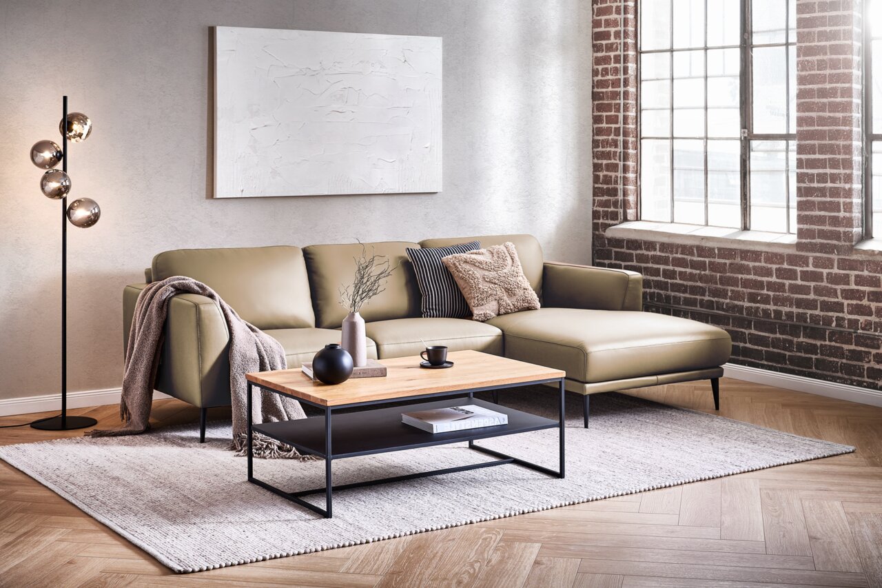 Moderne Longchairkombination in einem stilvollen Wohnzimmer mit Backsteinwand und großen Fenstern, aus der Perspektive von vorne fotografiert.