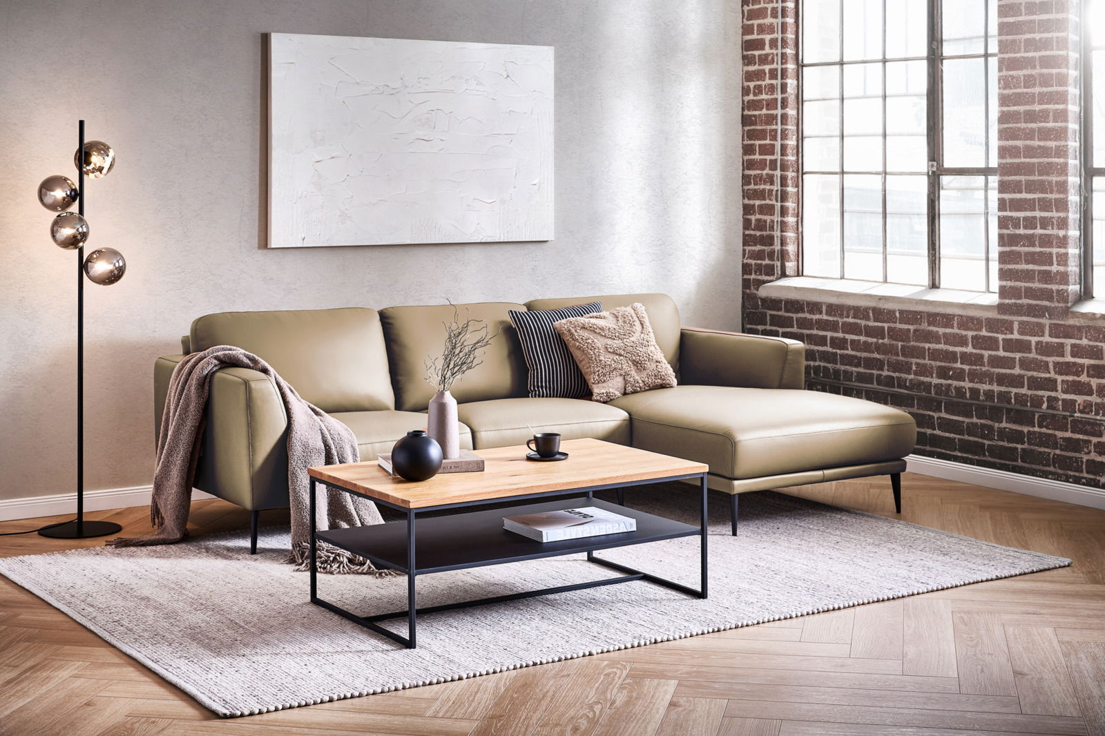 Moderne Longchairkombination in einem stilvollen Wohnzimmer mit Backsteinwand und großen Fenstern, aus der Perspektive von vorne fotografiert.