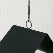 Nahaufnahme einer schwarzen Vogelfutterstation Solto, die an einer Kette hängt, mit einem weißen Ziegelhintergrund.