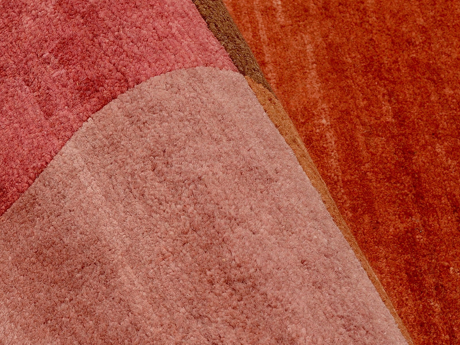 Nahaufnahme eines Wollteppichs mit verschiedenen Rottönen und geometrischen Mustern.