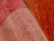 Nahaufnahme eines Wollteppichs mit verschiedenen Rottönen und geometrischen Mustern.