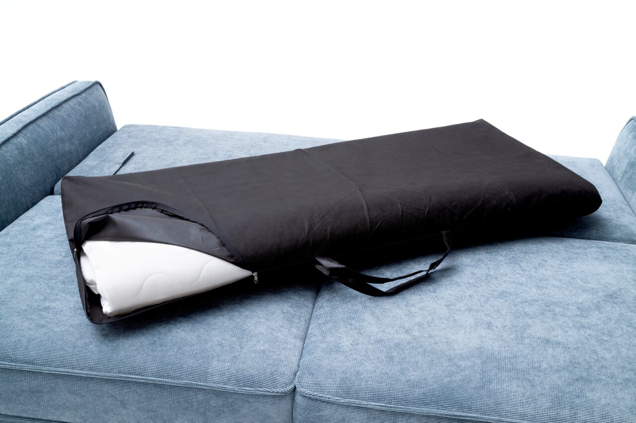 Schwarze Tragetasche mit Reißverschluss und Tragegriff auf einem blauen Funktionssofa, perspektivisch von oben fotografiert.