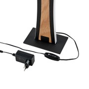 Nahaufnahme der Basis einer modernen Tischlampe mit schwarzem Metallfuß und Holzdetail, inklusive Netzkabel, Netzteil und Inline-Schalter (schräge Seitenansicht von unten)