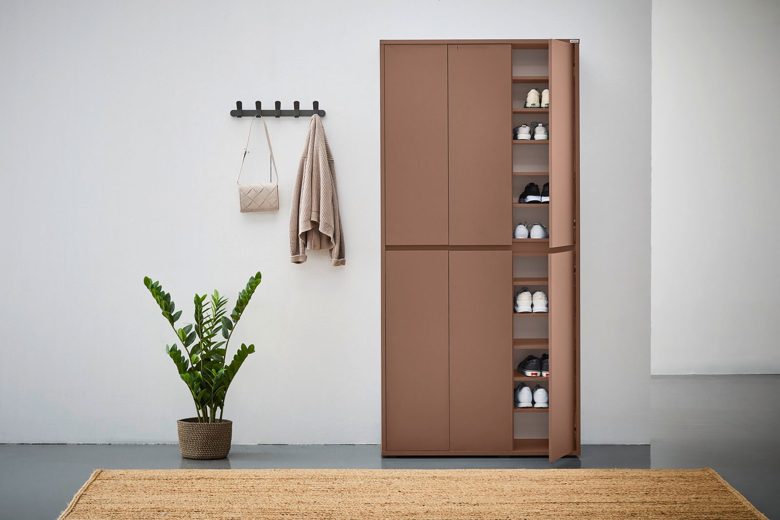 XXL-Schuh- und Mehrzweckschrank in brauner Farbe, teilweise geöffnet, mit mehreren Regalböden voller Schuhe, in einer modernen Wohnumgebung mit Pflanze und Wandhaken. Frontalansicht.
