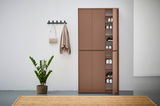 XXL-Schuh- und Mehrzweckschrank in brauner Farbe, teilweise geöffnet, mit mehreren Regalböden voller Schuhe, in einer modernen Wohnumgebung mit Pflanze und Wandhaken. Frontalansicht.