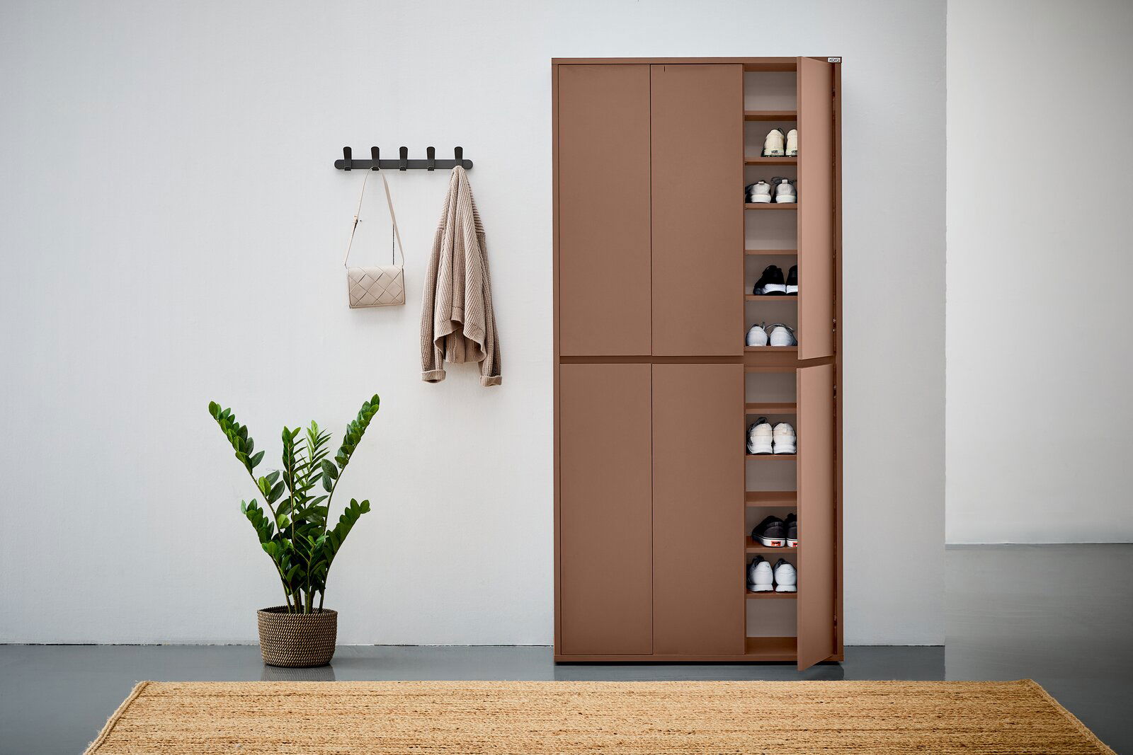 XXL-Schuh- und Mehrzweckschrank in brauner Farbe, teilweise geöffnet, mit mehreren Regalböden voller Schuhe, in einer modernen Wohnumgebung mit Pflanze und Wandhaken. Frontalansicht.
