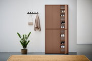 XXL-Schuh- und Mehrzweckschrank in brauner Farbe, teilweise geöffnet, mit mehreren Regalböden voller Schuhe, in einer modernen Wohnumgebung mit Pflanze und Wandhaken. Frontalansicht.
