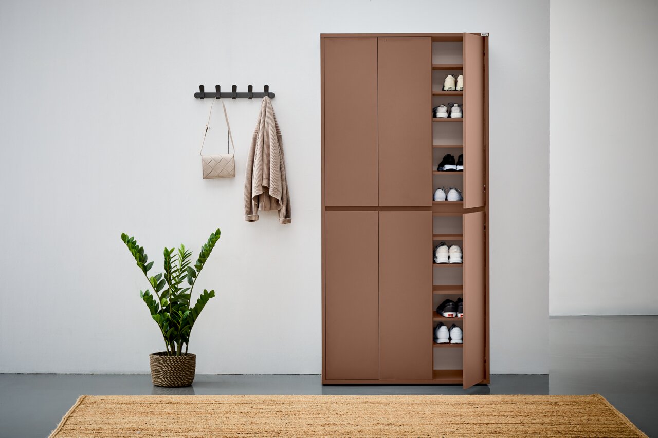 XXL-Schuh- und Mehrzweckschrank in brauner Farbe, teilweise geöffnet, mit mehreren Regalböden voller Schuhe, in einer modernen Wohnumgebung mit Pflanze und Wandhaken. Frontalansicht.