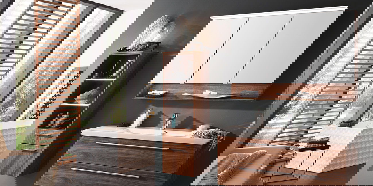 Bad mit braunen Möbeln, weißer Wanne und großem Fenster mit Holz-Lamellen.