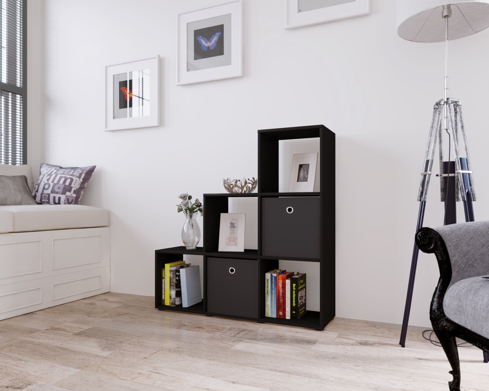Schwarzes, stufenförmiges Regalwürfel-Regalsystem mit offenen Fächern und zwei Stoffboxen, dekoriert mit Büchern, Bilderrahmen und Vase im hellen Wohnzimmer Perspektive: frontale Ansicht leicht von links.