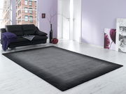 Moderner grauer Wollteppich in einem stilvollen Wohnzimmer mit schwarzem Sofa und lila Akzenten, aus der Perspektive des Raumes betrachtet.