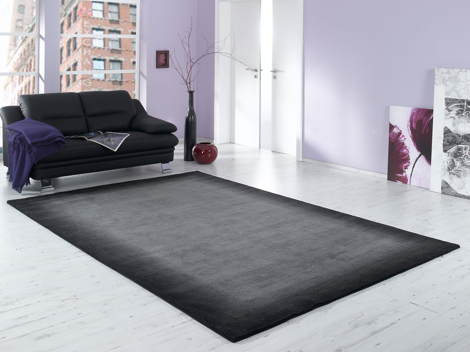 Moderner grauer Wollteppich in einem stilvollen Wohnzimmer mit schwarzem Sofa und lila Akzenten, aus der Perspektive des Raumes betrachtet.