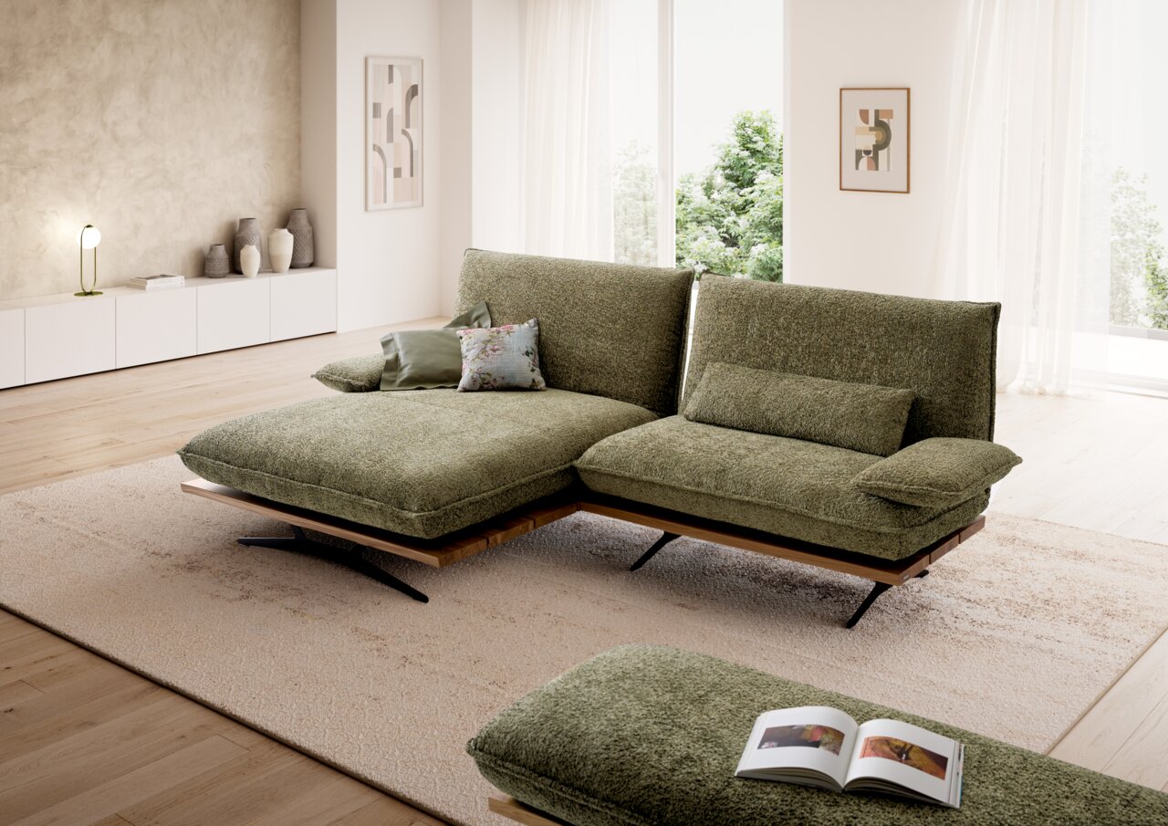 Moderne, olijfgroene stoffen hoekbank met chaise longue en zwarte metalen poten in een lichte woonkamer, van voren gefotografeerd in een licht schuin perspectief