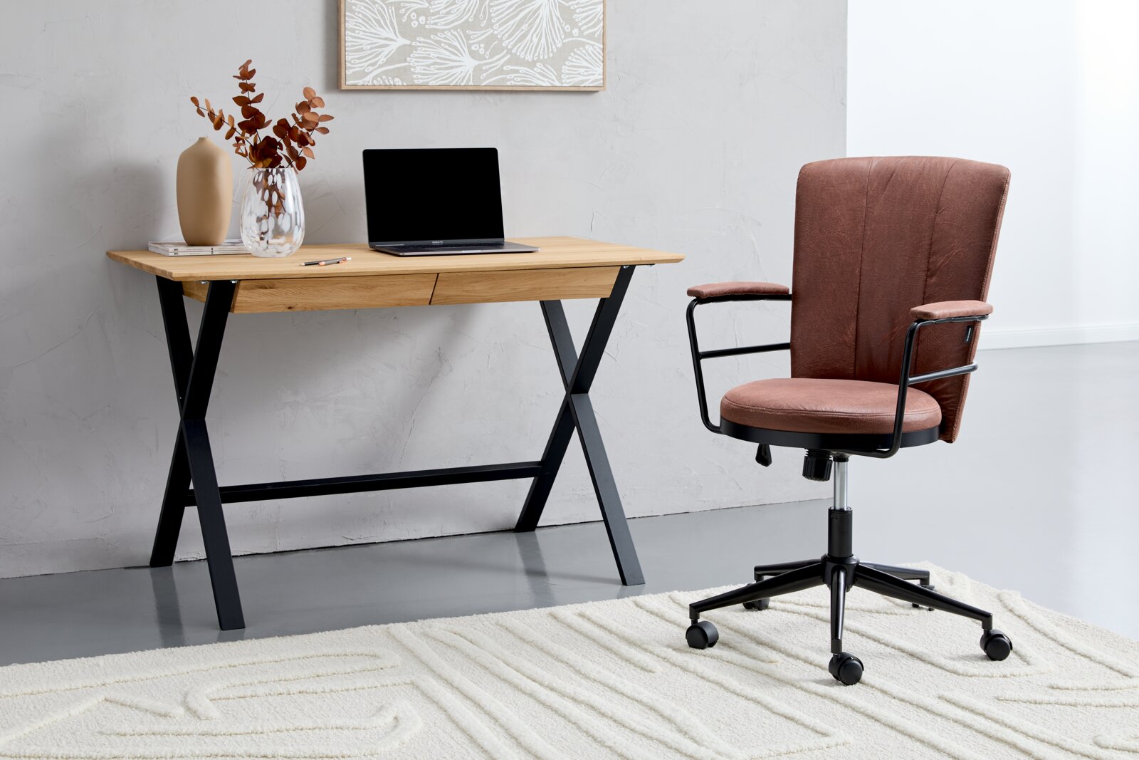 Modern bureau met houten blad en zwart metalen onderstel, gezien vanaf de zijkant, versierd met een vaas en een laptop, met daarnaast een gestoffeerde bureaustoel op een tapijt.