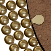 Nahaufnahme eines runden Spiegels mit goldenen, kuppelförmigen Verzierungen am Rand, von der Seite betrachtet.