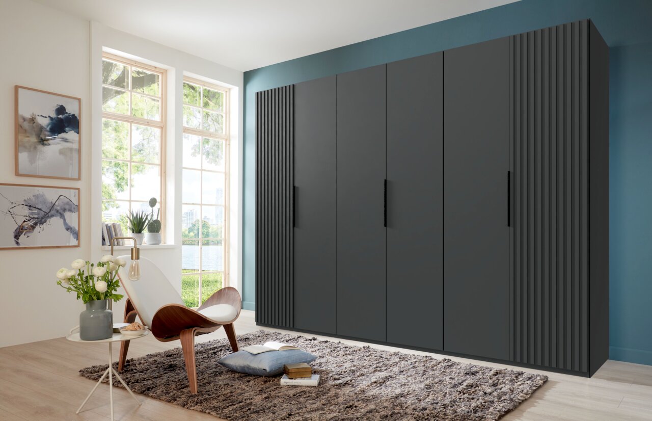 Z2 Drehtürenschrank 6-türig ANDORRA Moderner, sechstüriger Drehtürenschrank in dunklem Design, frontal fotografiert in einem stilvoll eingerichteten Raum mit großen Fenstern.