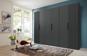 Moderner, sechstüriger Drehtürenschrank in dunklem Design, frontal fotografiert in einem stilvoll eingerichteten Raum mit großen Fenstern.