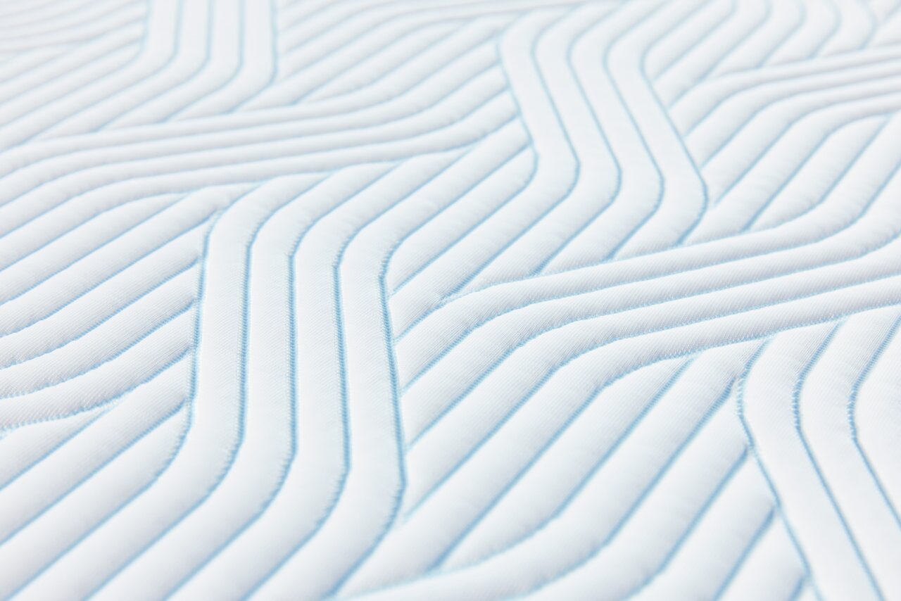 Tempur Topper Soft PRO PLUS SMARTCOOL Nahaufnahme eines gesteppten Matratzentoppers mit einem modernen, wellenförmigen Muster in Weiß und Hellblau.