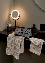 Gästetücher mit Leopardenmuster und JOOP!-Logo, drapiert auf einem Waschtisch neben einem beleuchteten Spiegel, aus seitlicher Perspektive.
