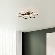 Moderne LED-Deckenleuchte in Blütenform mit fünf ovalen Leuchtringen in Schwarz/Weiß, warmweiß leuchtend, an weißer Zimmerdecke montiert, Perspektive von unten im Raum