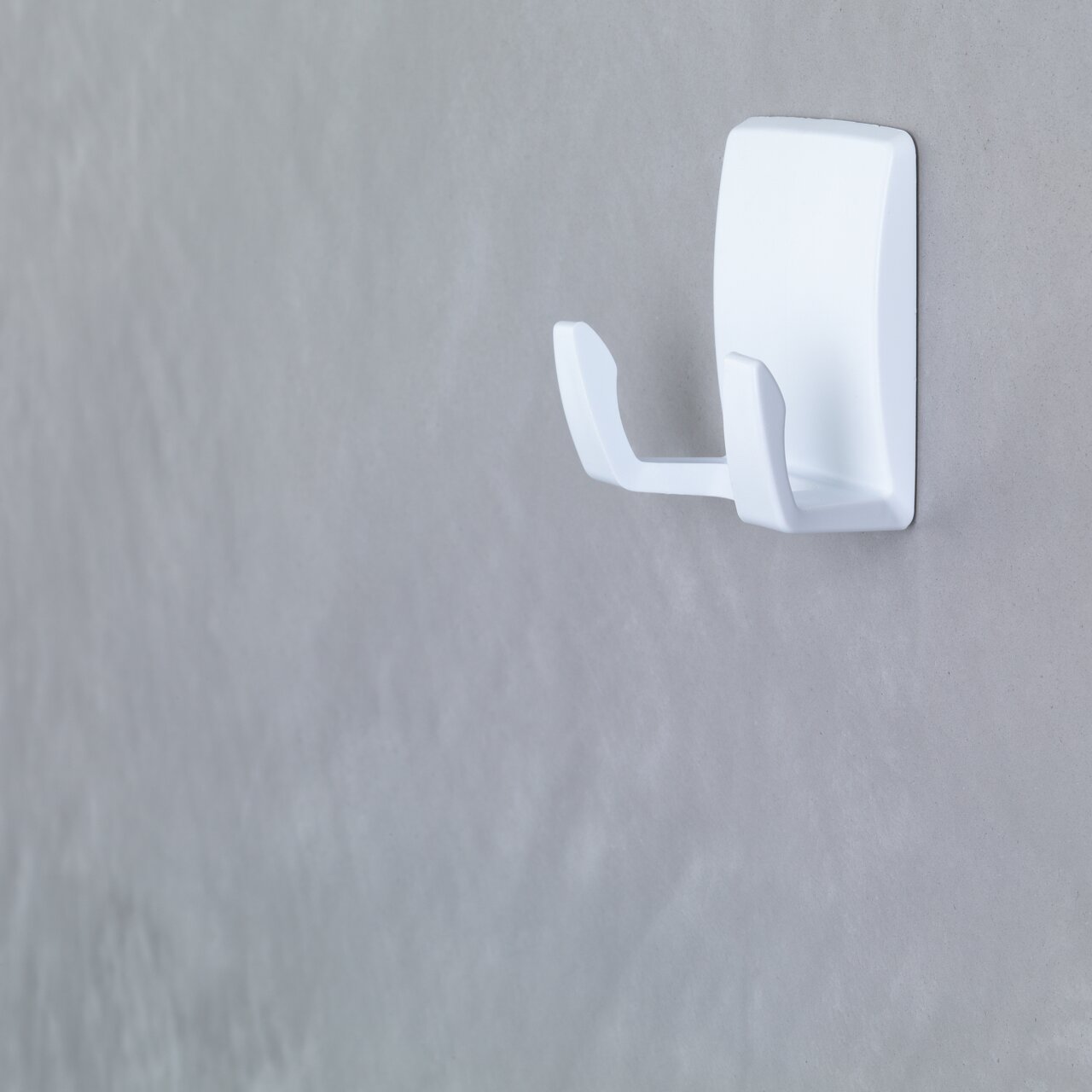 Weiße Wandhakenhalterung, seitliche Perspektive, an einer grauen Wand montiert.