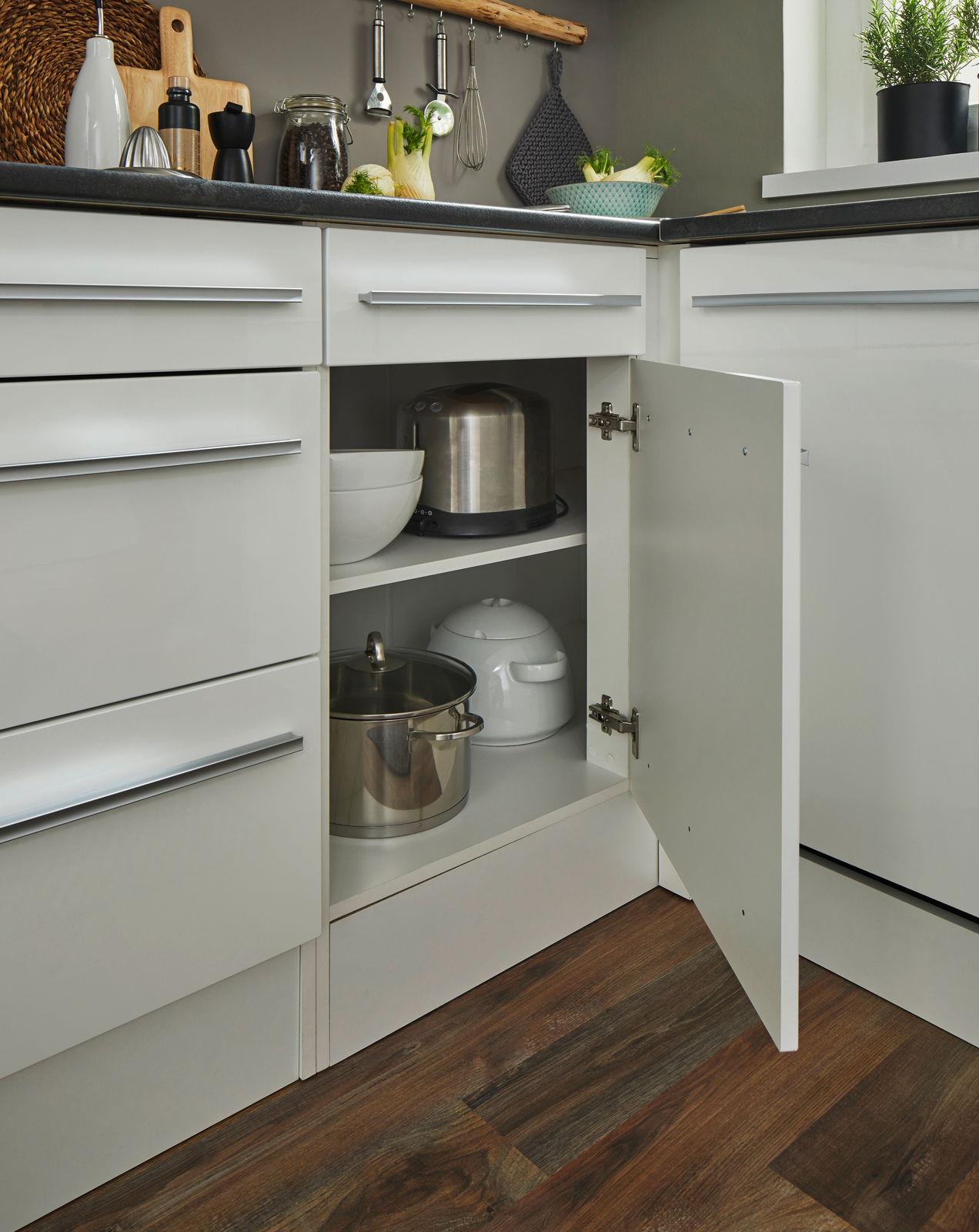 Eckunterschrank in einer modernen Küche, geöffnet, mit Töpfen und Schüsseln auf zwei Regalböden, aus der Perspektive von vorne rechts.